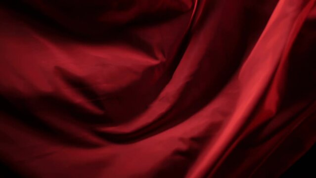 The chic and elegant texture of the moving folds of light red fabric on a black background under dramatic lighting. Slow Motion 200 FPS