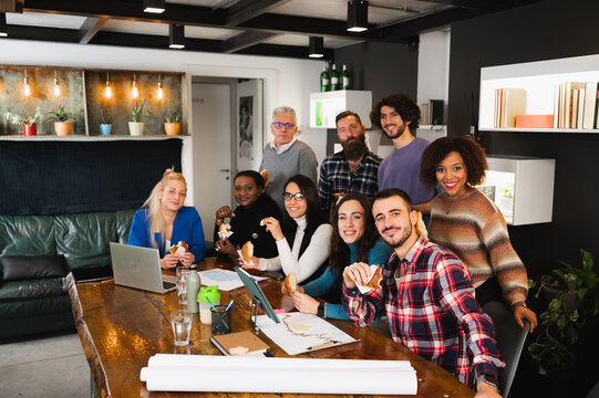 Large group of colleagues or students with different ethnicity sitting at desk using computer and having a break. People looking at camera.
