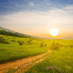 Obraz premium ground road among green mountain valley at the sunset