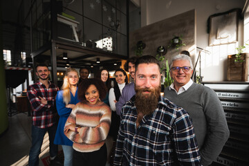 Portrait of casual and mixed trace group of colleagues in a modern office standing looking at camera smiling.