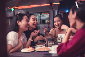 Young Asian women laughing as they have a good time catching up over dinner at an outdoor restaurant. Showing positive relationship with friends.