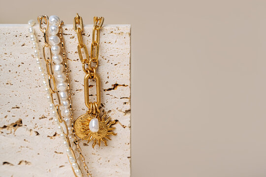 Trendy jewelry with chains, pearl necklace and pendant shapes moon and sun. Stylish golden bijouterie on the stone. Fashion accessories.