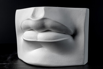 Plaster lips. A fragment of a plaster sculpture of a human face on a black background.