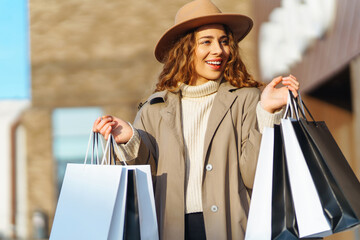 Stylish woman with shopping bags walks through the city streets. Spring Style. Consumerism, purchases, shopping, lifestyle concept.