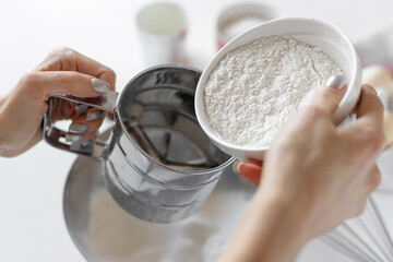 closeup of female hands sifting flour through sieve. cooking pasta, pizza or bread. selective focus