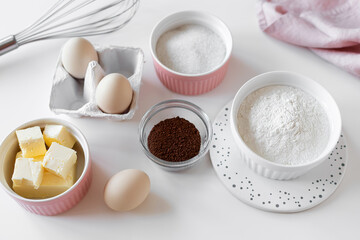 Top view bake ingredients on a white table. Bowls with flour, butter, sugar, cocoa powder and eggs. Baking concept