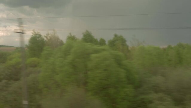 view from window of high-speed train on landscape of beautiful nature wild field and forest on evening cloudy dusk sky sunset in summer background. Transport, travel, railway, communication concept