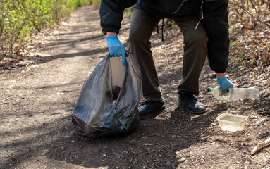 Man in gloves collects plastic trash in forest