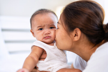 Mom happy joyful teasing asian infant baby new born sitting on bed and kiss her