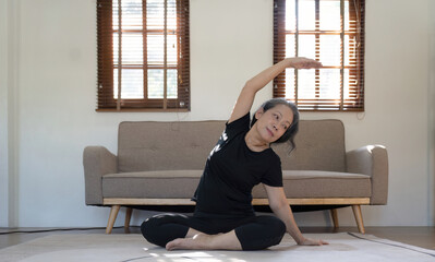 Healthy and elderly woman in workout clothes practicing yoga in her living room