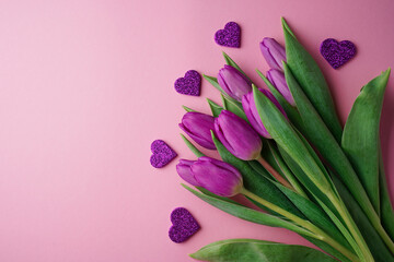 Bouquet of purple tulips with hearts on rose background. Mothers day, Valentines Day, Birthday celebration concept. Greeting card. Copy space, top view