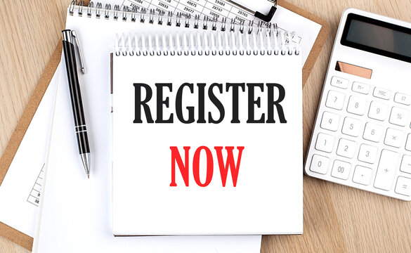 REGISTER NOW is written in white notepad near a calculator, clipboard and pen. Business concept