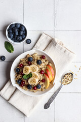 Oatmeal with fruits and berries lies in a white plate, which stands on a white background.