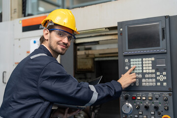 Male engineer operating cnc machine in control panel at factory. Smiling man technician in uniform and helmet safety working at workshop heavy metal industrial