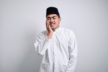 Asian muslim man in white clothes touching his cheek suffering from toothache