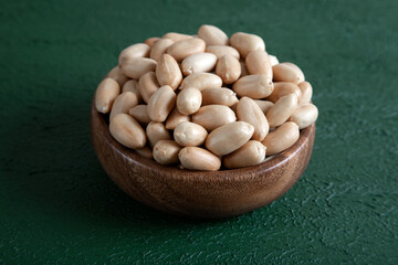 Bowl full of roasted peeled peanuts on green background

