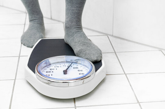 Feet in socks stepping on a personal scale on the tiled bathroom floor to measure the body weight, copy space