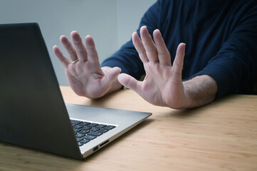 Hands in defensive gesture against a laptop computer, avoiding further work on a hacked system or other danger and offence, online risk in business and privacy, copy space, - obrazy, fototapety, plakaty