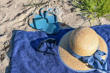 Straw hat, sunglasses and flip-flops on a blue towel on a natural beach near the tourist resort...
