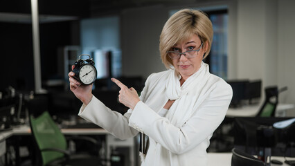 Naklejka na ściany i meble Caucasian business woman showing on alarm clock in office. 
