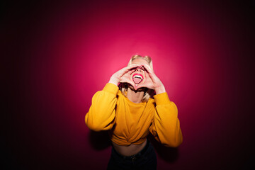 A goofy girl standing in front of the magenta background and sticking her tongue out. Viva magenta.