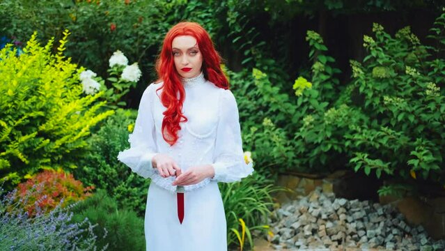 fantasy art portrait red-haired evil woman warrior, halloween makeup red bloody scars on face. Vintage white dress. Summer green trees. Gothic girl holds dagger weapon in hands plays with edge knife
