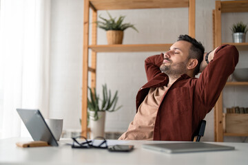 Fototapeta premium Caucasian millennial business man manager resting after hard work in home office during the day with hands behind the back of the head, looking carefree and relaxed.
