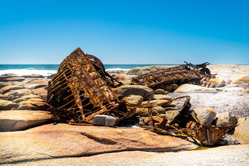 A rusty shipwreck lies on stones on the coast