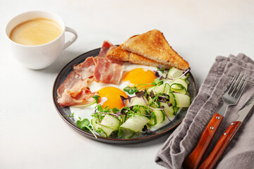 Continental breakfast - eggs, bacon, micro greens and cucumber slices on a plate on the table....
