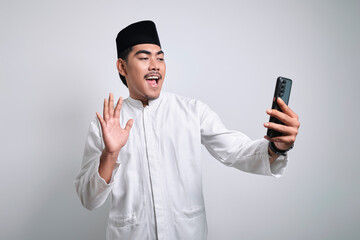 Cheerful young Asian Muslim man doing video call or selfie shot on mobile phone