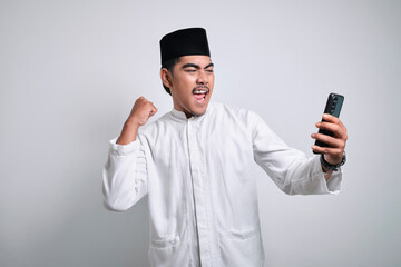 Asian muslim man in white clothes holding smartphone doing winning gesture holding mobile phone