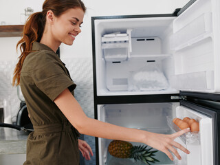 Fototapeta na wymiar A woman opened the refrigerator smiles looking into it, thinking what to cook, defrosted the refrigerator, freezer repair in the kitchen at home, healthy eating, proper diet.
