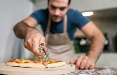 handsome chef cut delicious homemade italian mozzarella pizza after prepare and bake from stove or oven for lunch meal or dinner in local italian pizza restaurant