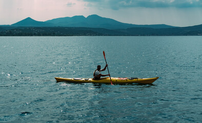 Messinia, Navarino Bay, Greece - 19 June 2022 : Canoe instructor or kayak water sportsman in water, mountains on background