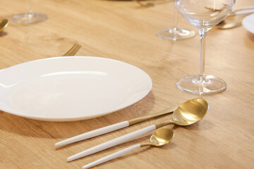 Dining table arrangement with white ceramic plates, silver flatware set with white handles and wine glasses