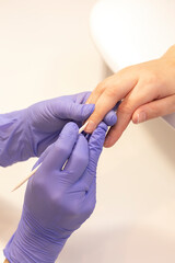 Manicure technician pushes back client cuticles, holding wooden cuticle remover in purple gloves.Eco Japanese beauty treatment of hands in process, procedure on workstation in treatment room.Vertical