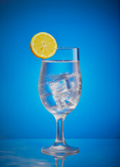 Gin and tonic with ice on a blue gradient background.
