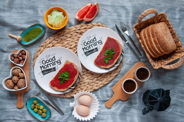 Coffee cups, mocha pot, two eggs, wheat bread, honey and lettuce for healthy breakfast spread on a table cloth. 