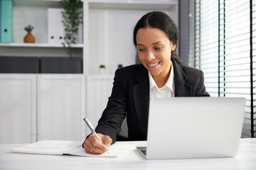 businesswoman using laptop computer and writing on notebook in the office