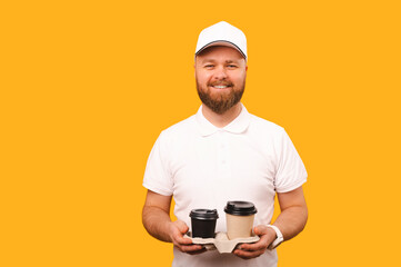 Hi I am a delivery man and have brought you some fresh hot coffee in two cups. Studio portrait of a bearded man over yellow backdrop.