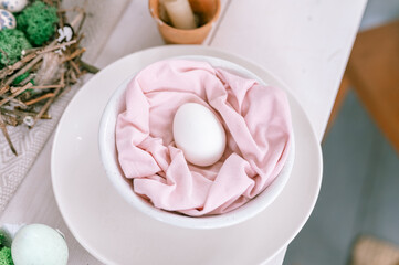 Fototapeta na wymiar happy easter holiday in springtime season. festive home decor. traditional food. natural white chicken egg in pastel pink fabric in a plate on the table