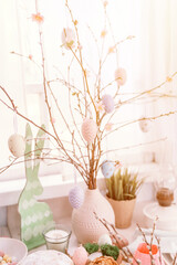 happy easter and spring holidays time. festive tablescape set decor. decorative rabbits or bunnies and tree branches in vase decorated with artificial eggs. pale pastel pink colors. flare