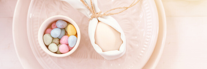 happy easter holiday in springtime. festive home decor. traditional food. white beige chicken egg wrapped in pale blue cloth like rabbit or bunny ears and small candy eggs on table. banner. flare