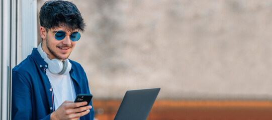 young man with mobile phone and laptop wearing sunglasses outdoors