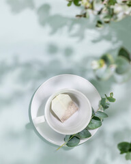 Organic tea concept. Empty cup with tea bag on blue background with eucalyptus green leaves and shadows. Healthy drink, natural herbal tea. Summer morning still life. Flat lay