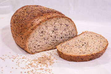 Still life with natural seed bread and a slice of it in clear bright light on a white cloth tablecloth
