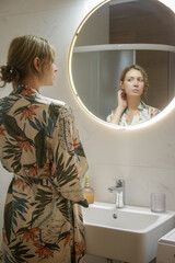 Young woman doing her morning or evening routine in the front of mirror in bathroom, personal...