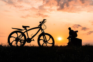 Obraz premium Silhouette of a man with a bicycle on a sunset background.