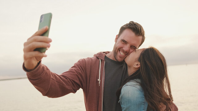 Couple in love hugging each other makes selfie while standing on the beach