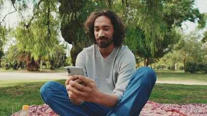 Young man using mobile phone while sitting on the lawn in the park